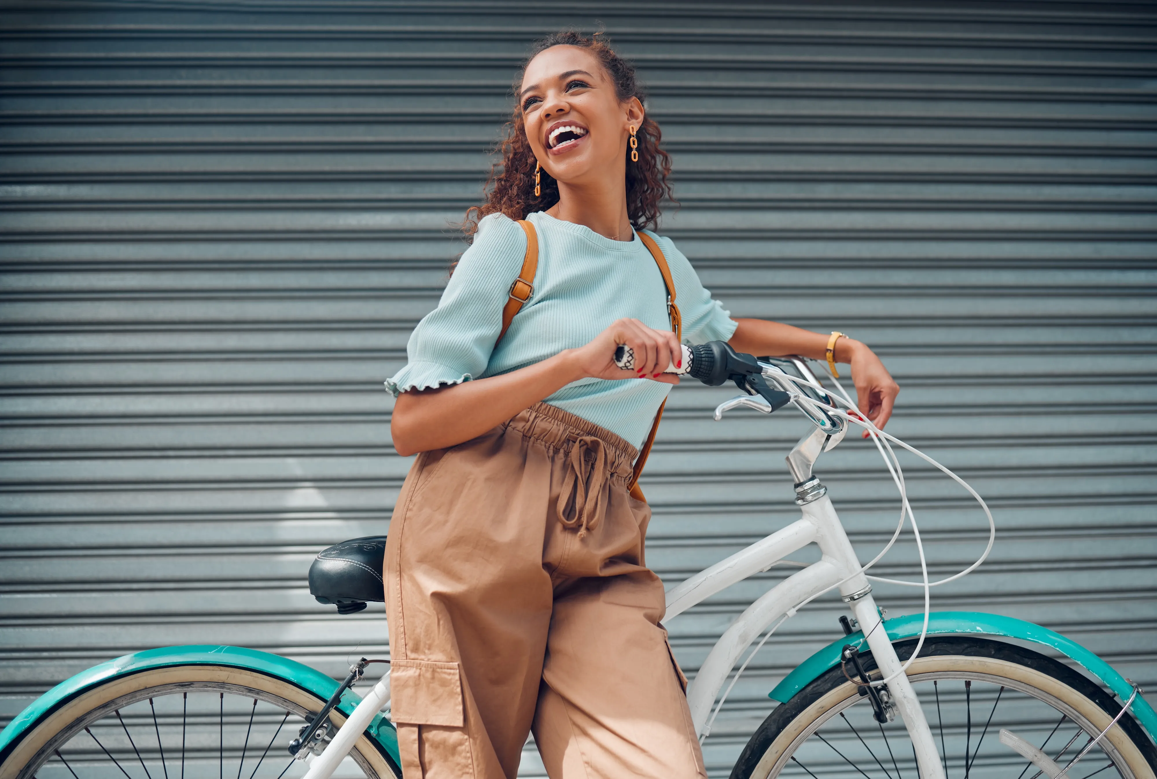 Young woman smiling while walking her bike near Meadowbrook Gardens apartments in Mansfield, CT, embracing an active and vibrant lifestyle