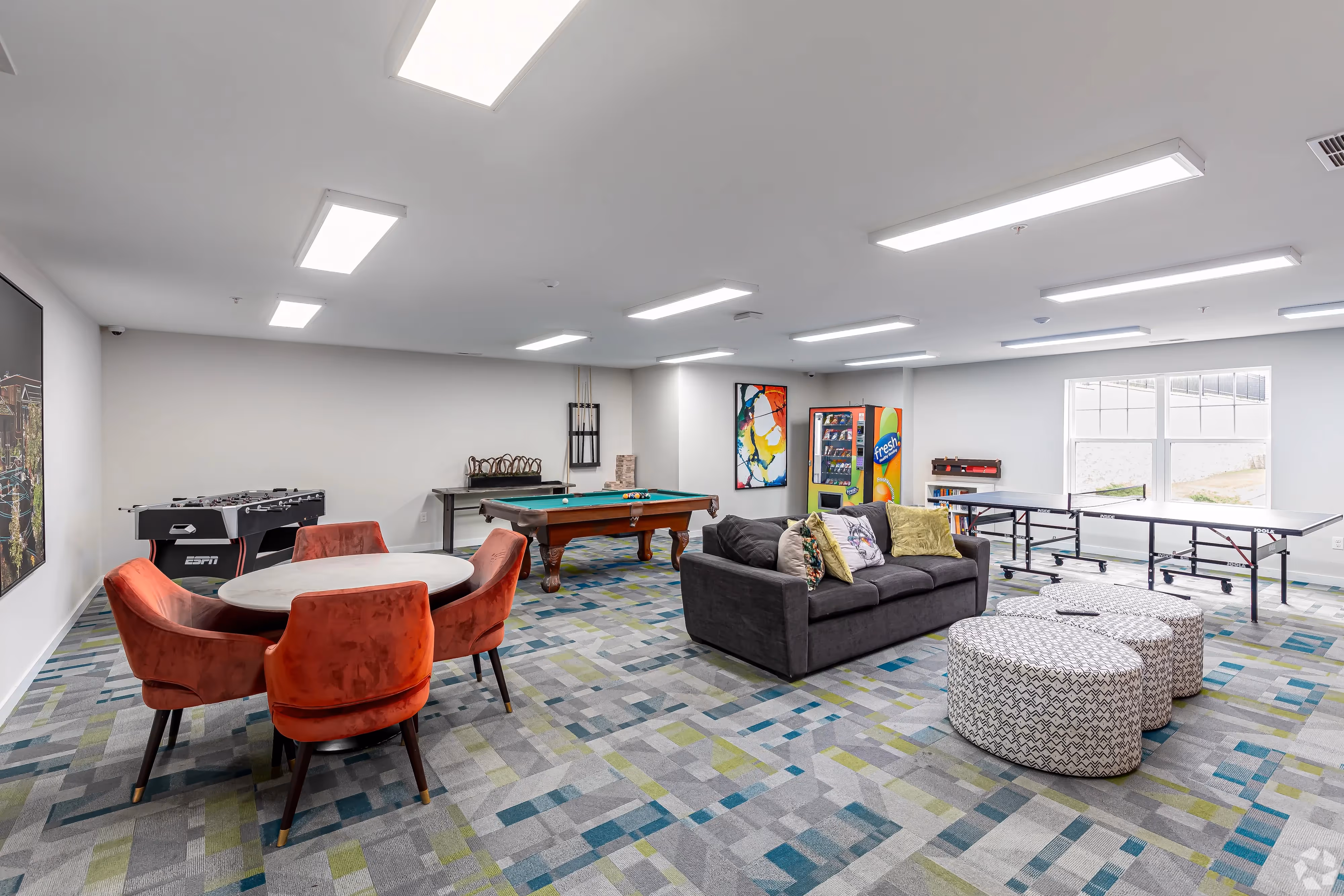 Spacious resident community room with a billiards table, foosball, ping pong, and comfortable seating, offering entertainment at Meadowbrook Gardens in Mansfield Center, CT.