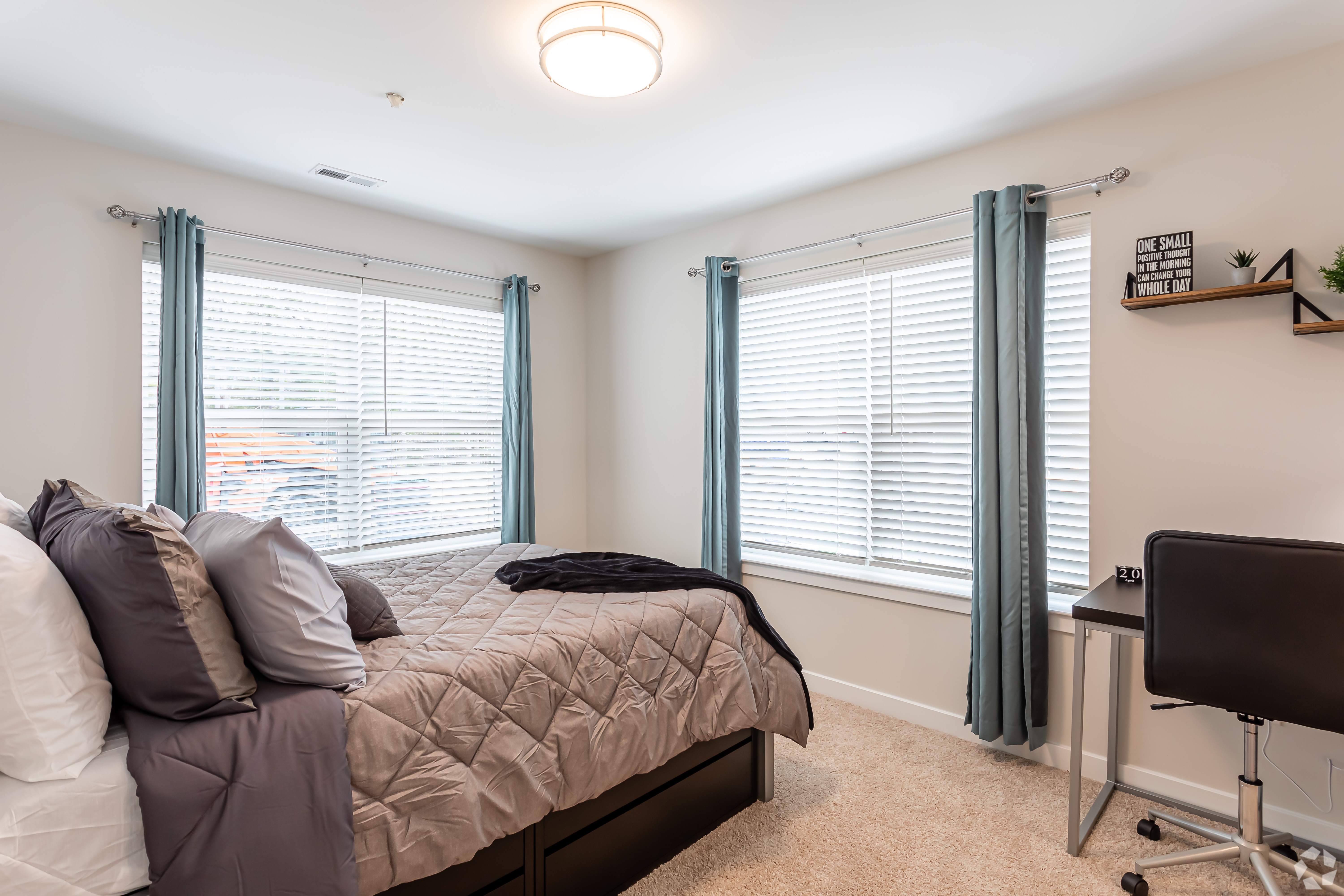 Furnished bedroom with bed and computer desk and two corner windows