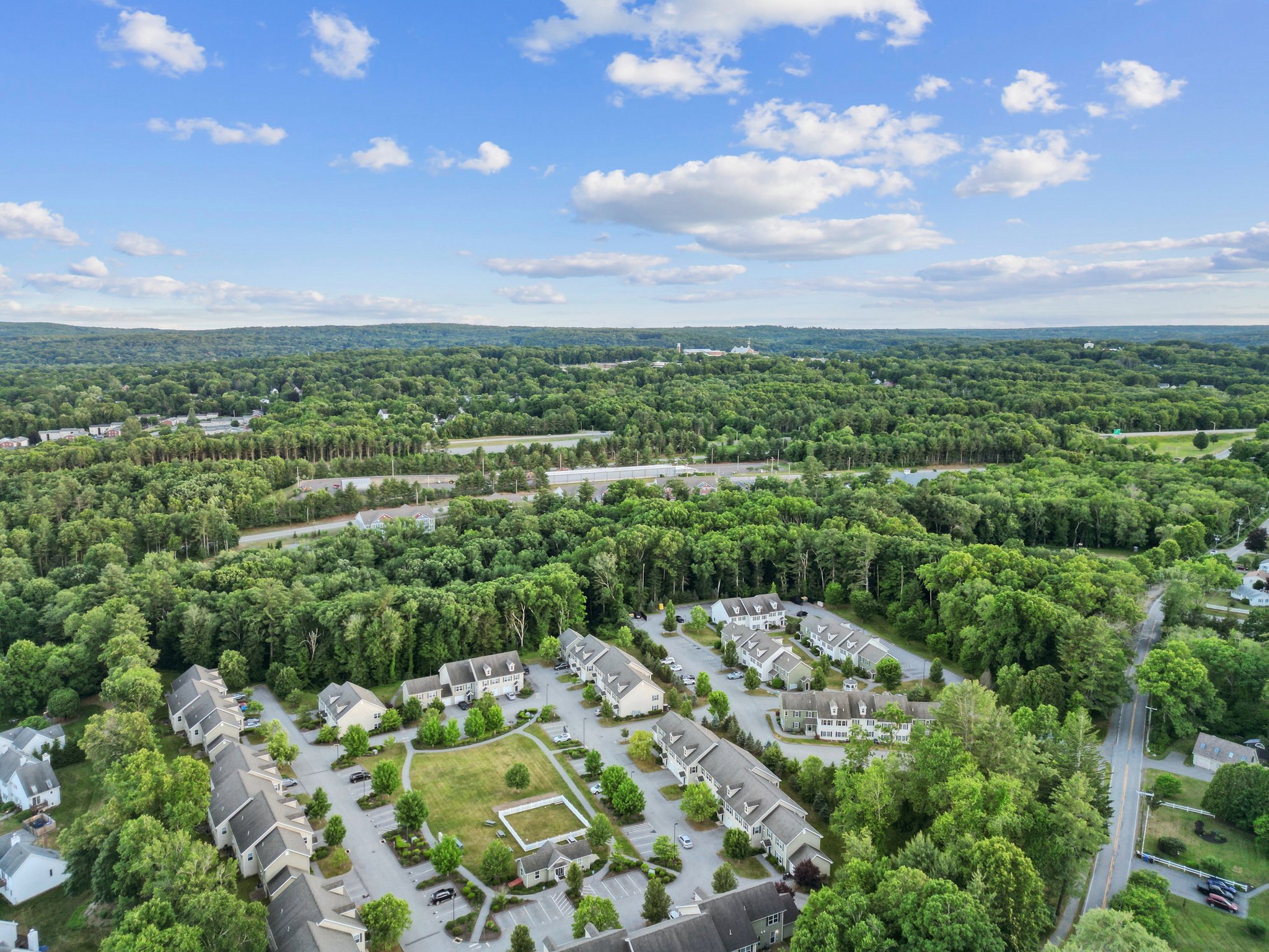 Exterior view of light-colored townhome-style apartment buildings with blue doors and black shutters, featuring dormer windows, at Meadowbrook Gardens in Mansfield Center, CT.