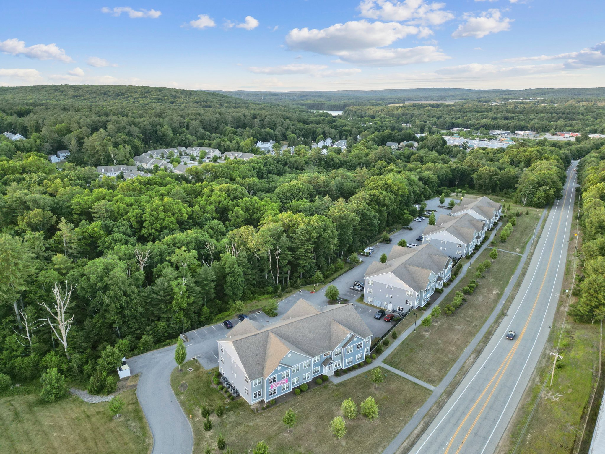 Residential street scene showing modern townhome apartment buildings with individual garages and parked cars, at Meadowbrook Gardens in Mansfield Center, CT.