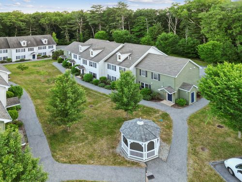 Aerial view of light-colored townhome apartment buildings with dormer windows and a white picket fence, at Meadowbrook Gardens in Mansfield Center, CT.