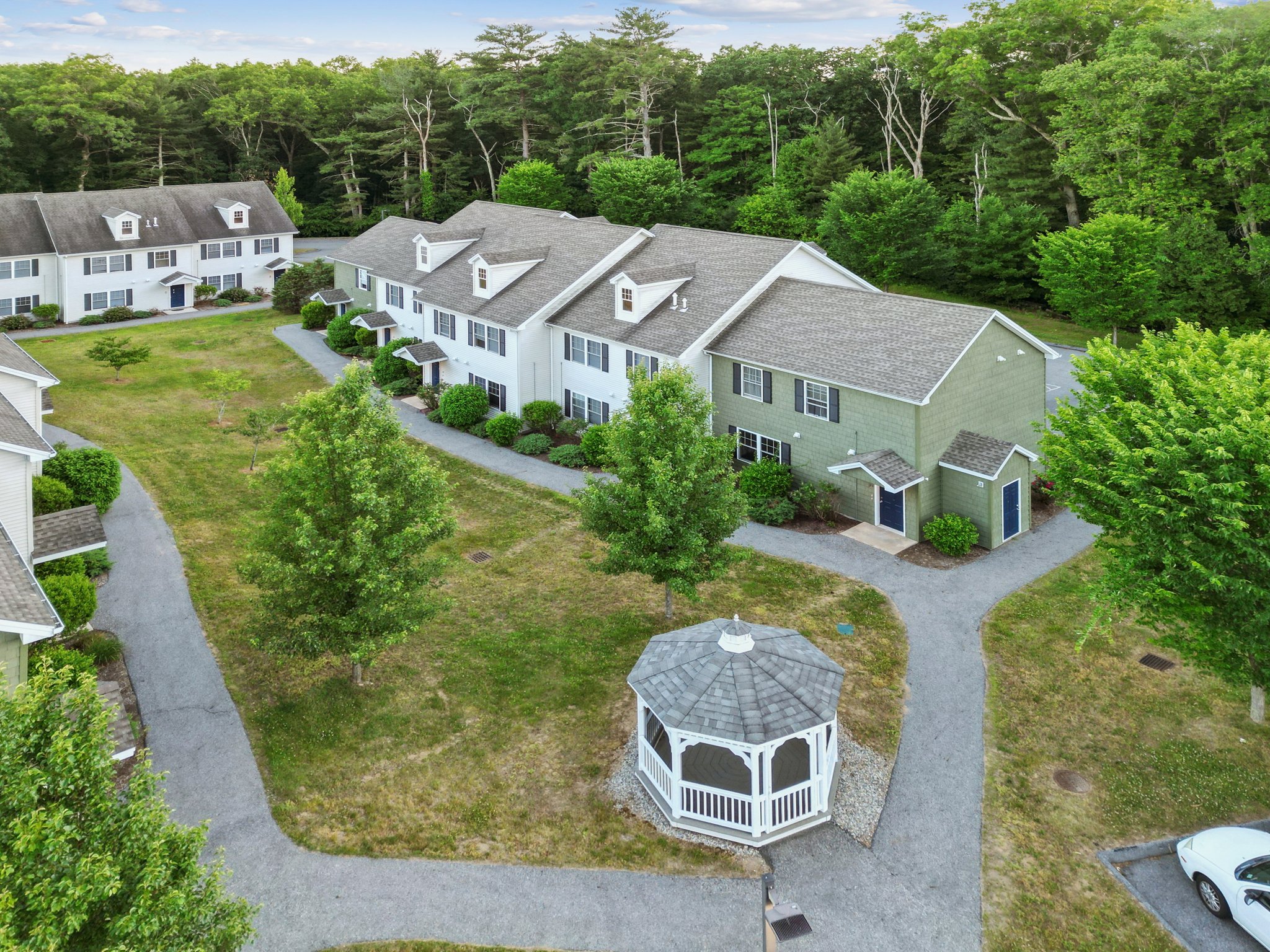 Aerial view of light-colored townhome apartment buildings with dormer windows and a white picket fence, at Meadowbrook Gardens in Mansfield Center, CT.