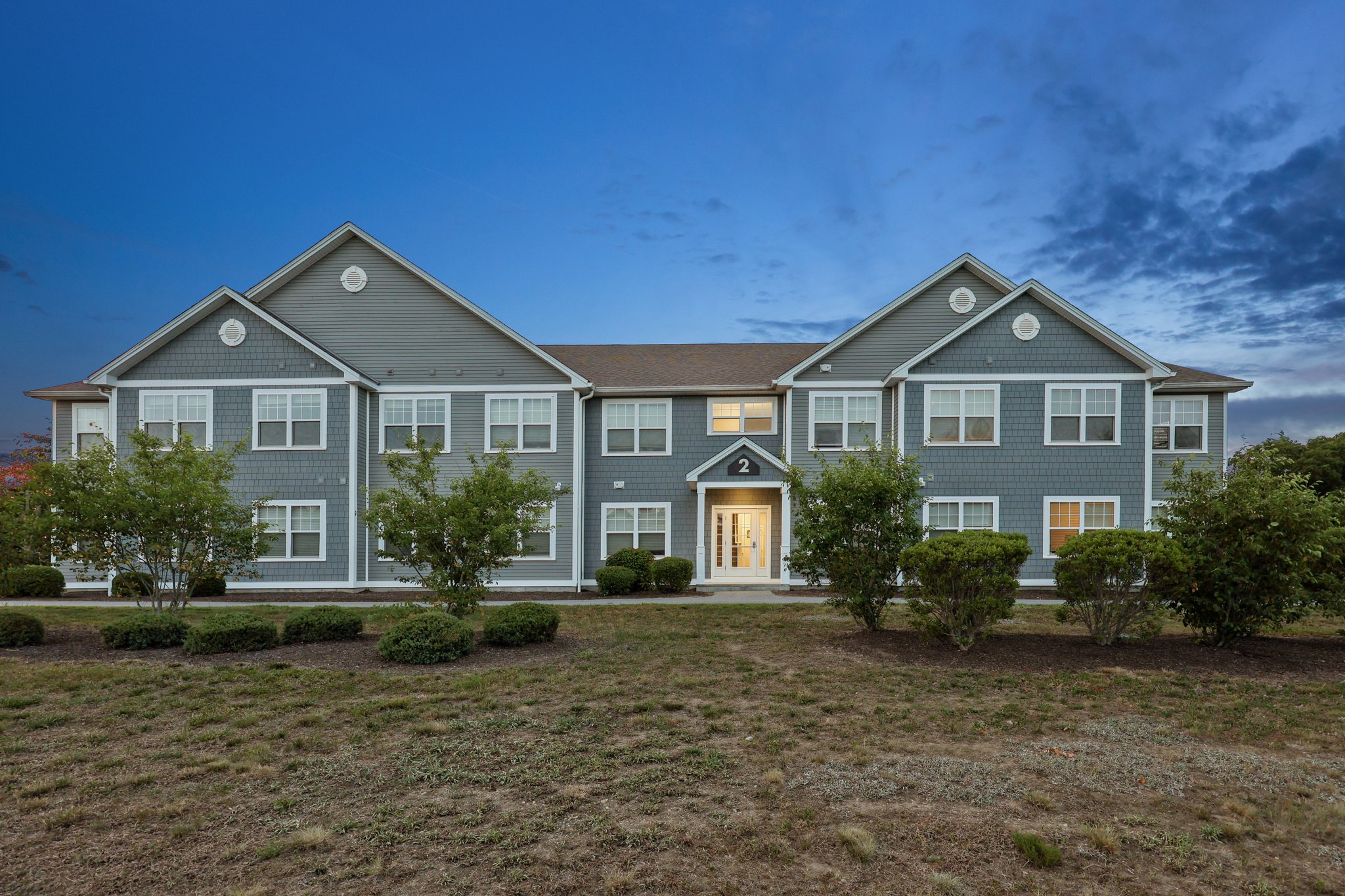Row of charming townhome-style apartment buildings with blue doors, set on a green hillside at Meadowbrook Gardens in Mansfield Center, CT.