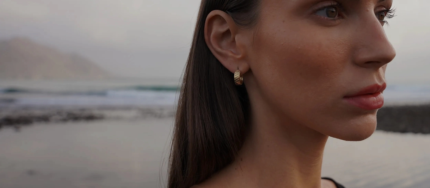 Close-up profile of a woman with gold earrings by the ocean