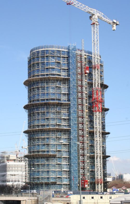 Independent scaffold structure with loading platforms and access stairs at a high-rise building construction site.