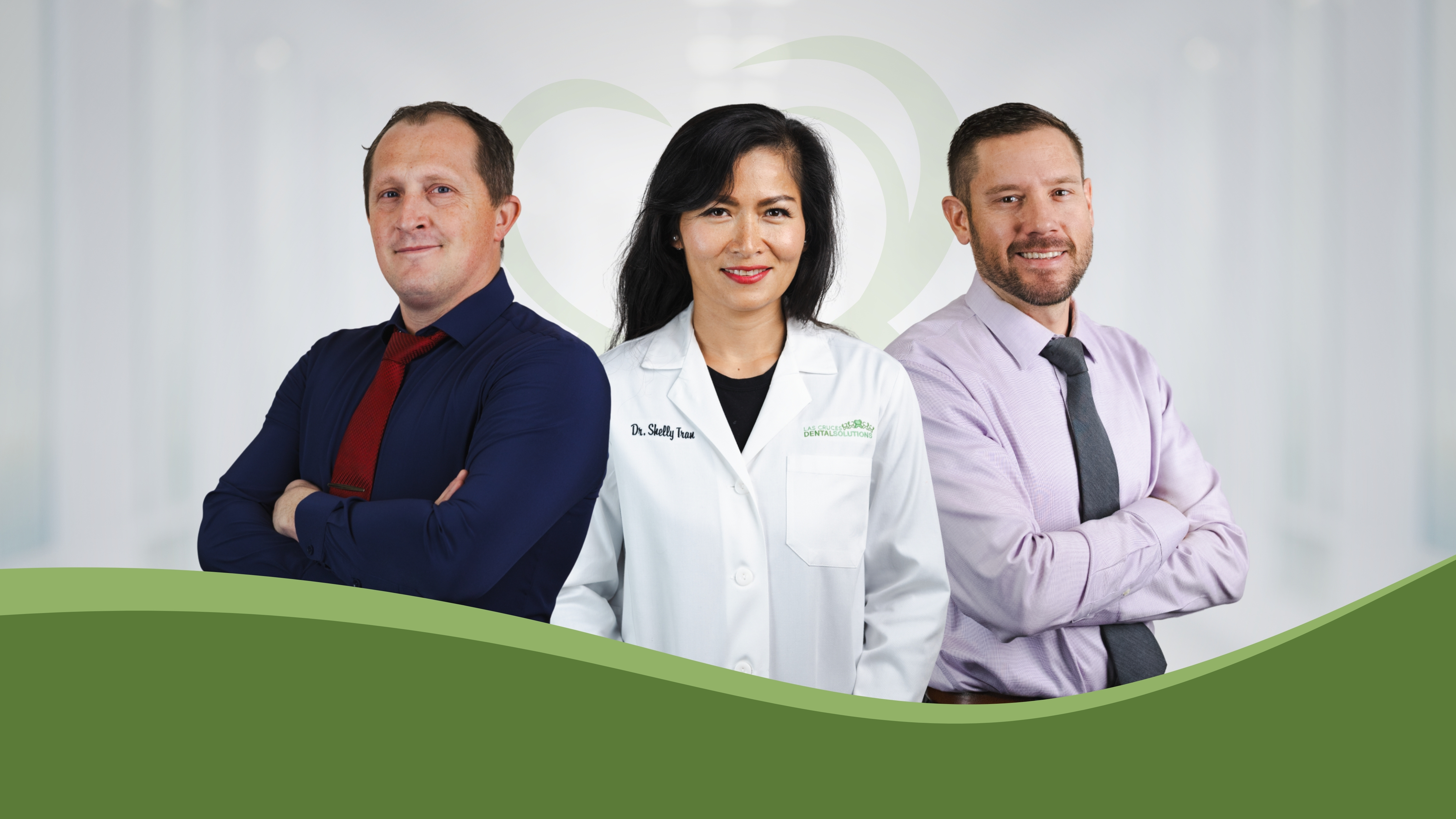 Three dental professionals standing side by side with arms crossed, one wearing a white lab coat and two in dress shirts and ties, smiling.