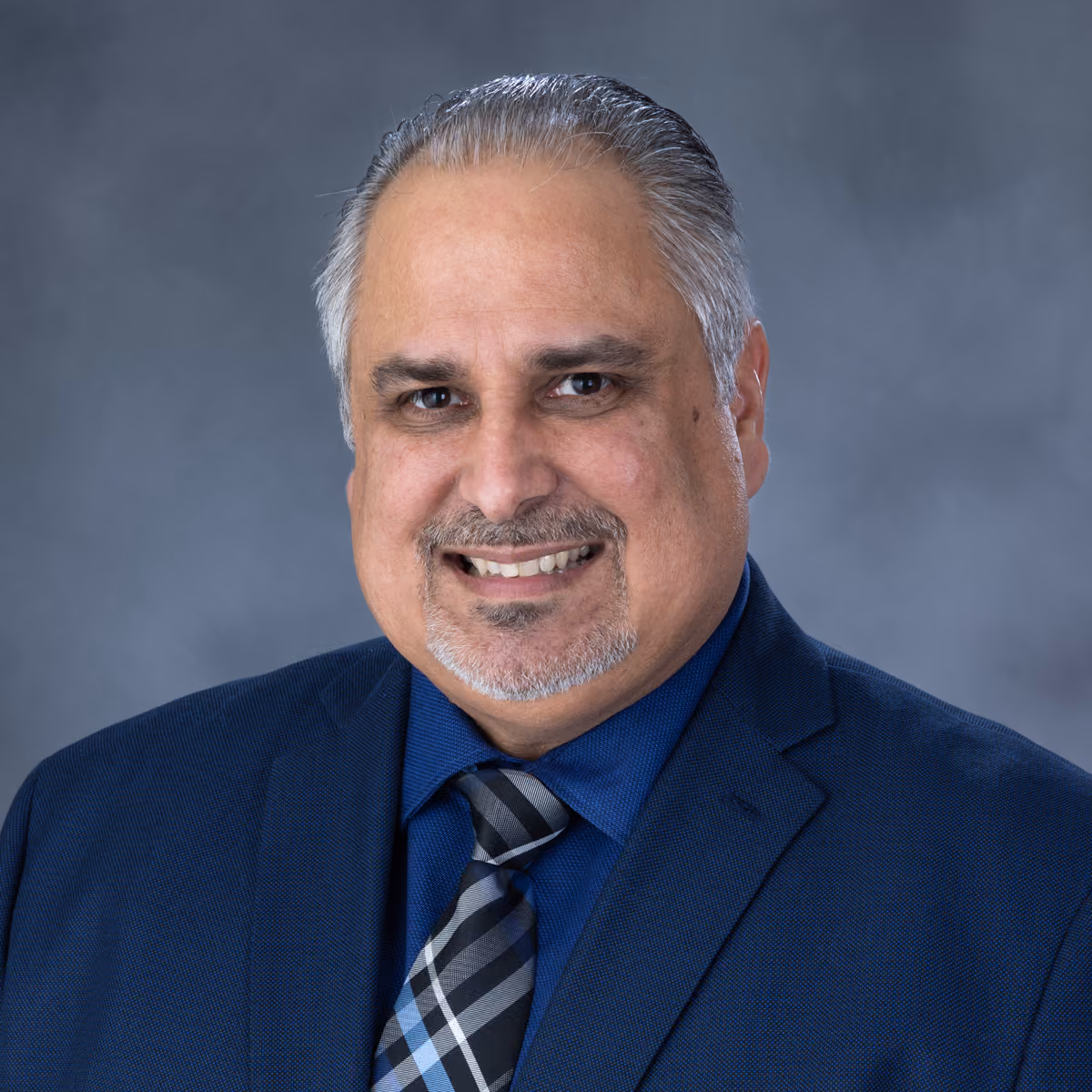 Smiling middle-aged man with gray hair, gray goatee, wearing a blue suit, shirt, and striped tie.