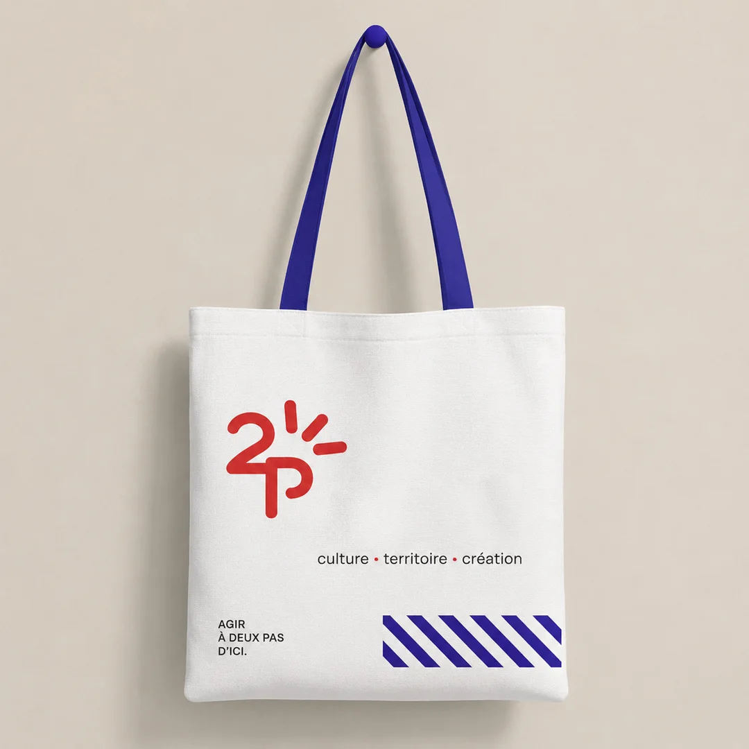 Bolsa de tela blanca con la identidad visual de A2PAS, logotipo rojo, asas azules y elementos gráficos de la marca.