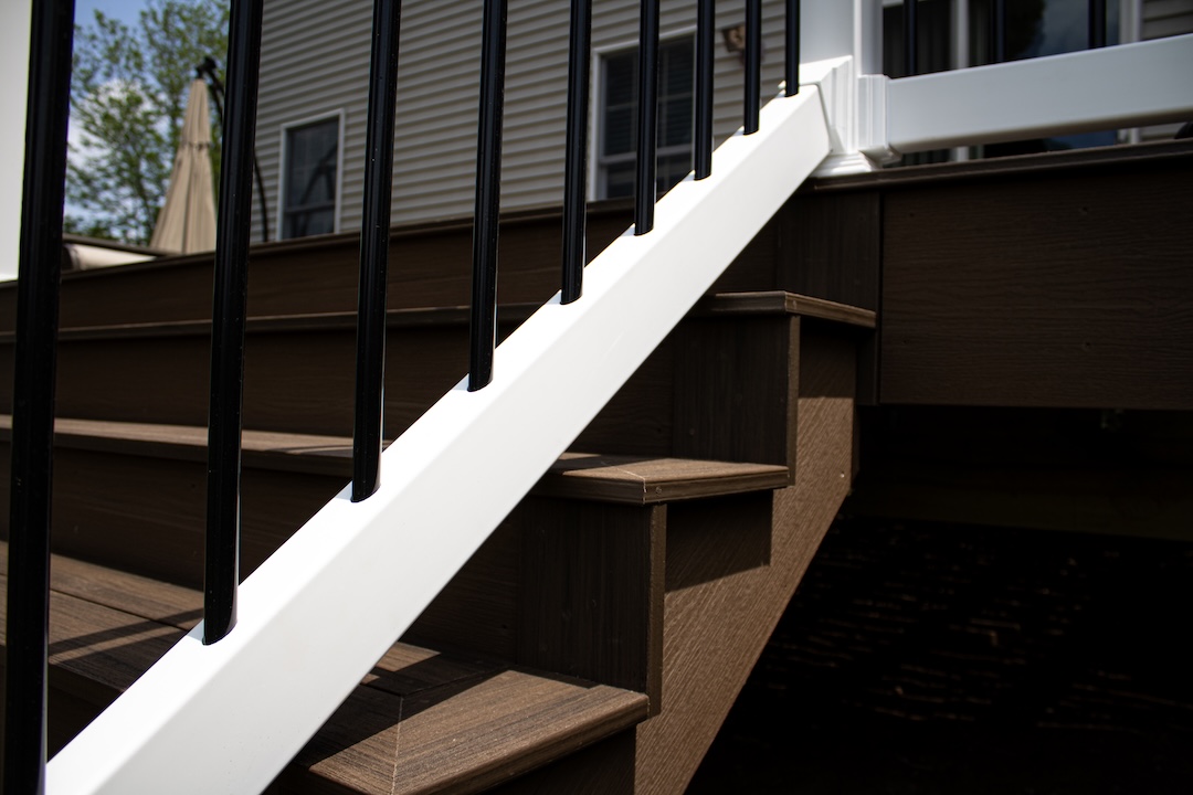 Close-up of deck stairs with brown composite steps and a white railing with black balusters