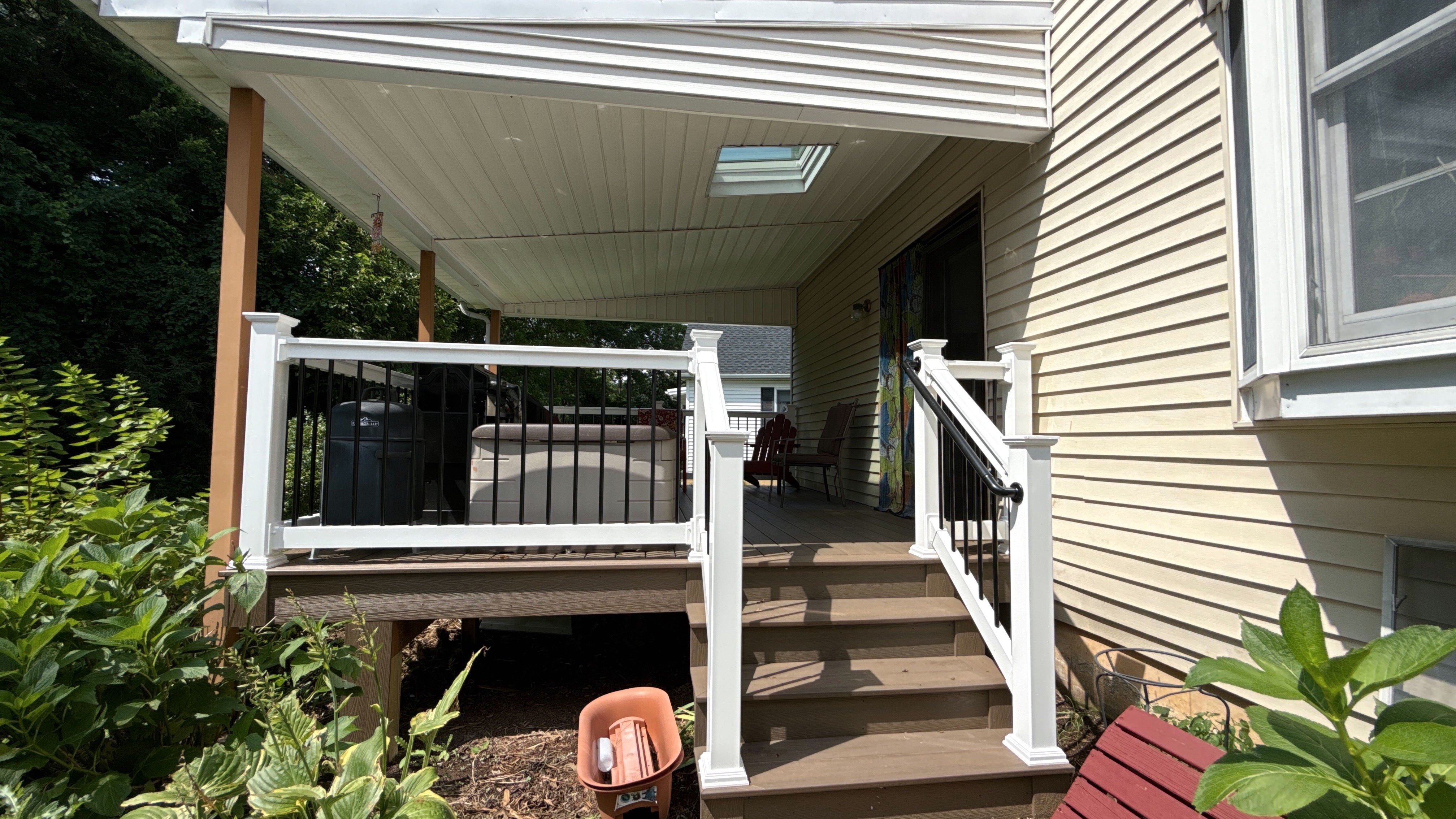 After photo of a deck surface replacement in Bethlehem, PA, featuring Sandbar composite decking, white vinyl railings with black aluminum balusters, and matching stairs under a covered roof with skylight.
