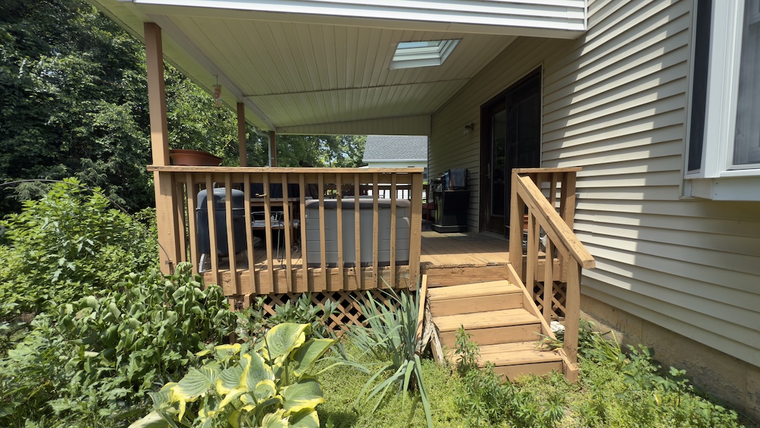 Before photo of a weathered wooden deck, featuring natural wood boards, vertical railing spindles, and a covered roof structure with a skylight.