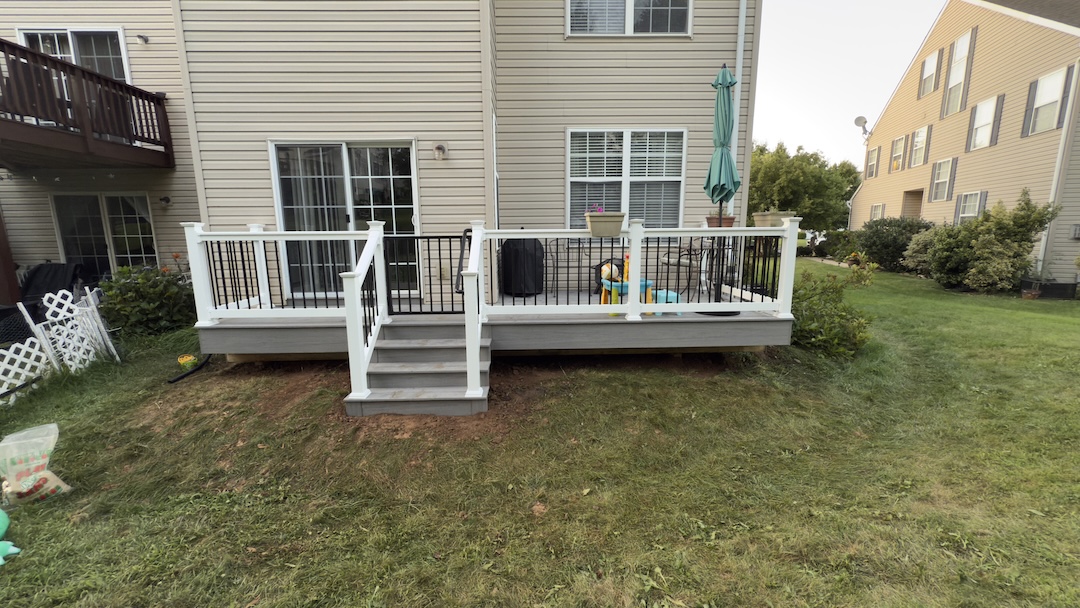 Gray composite backyard deck with white vinyl railing, black balusters, and centered stair set
