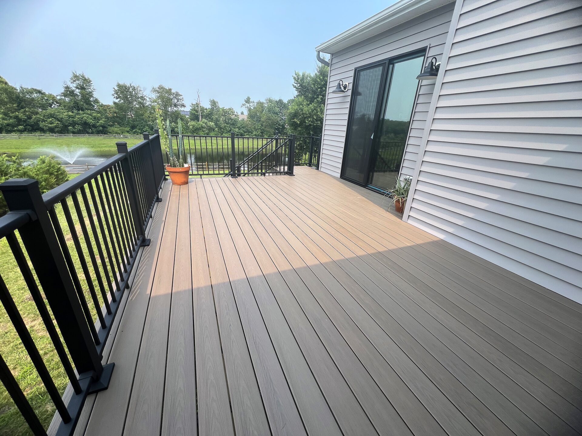 New composite deck with Deckorators Venture Sandbar decking and black aluminum railing overlooking a pond in Swedesboro, NJ.