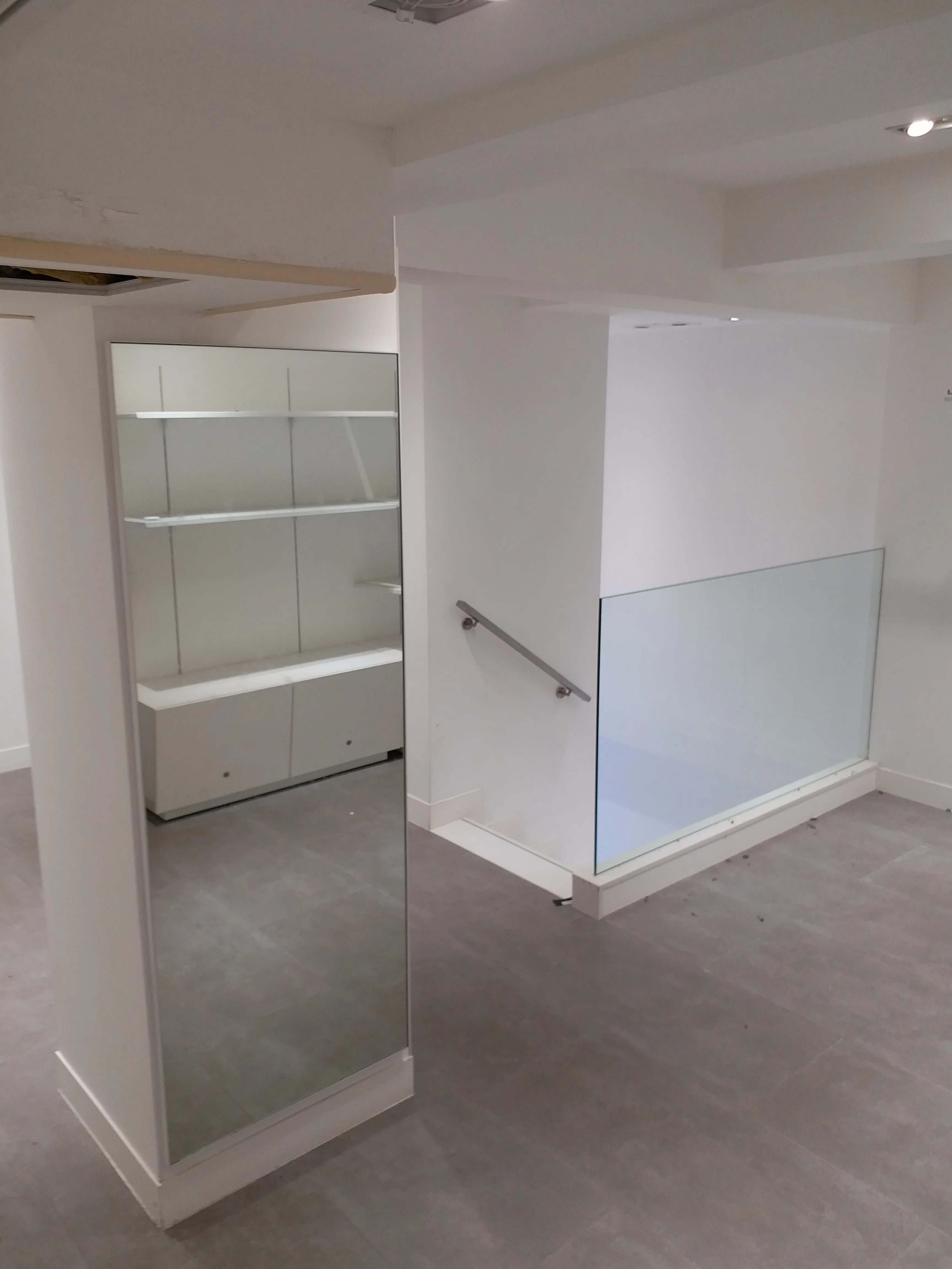 Ref#2992 is a clean, empty space perfect to rent for a shop or office, with light gray floors, white walls, a large mirror, glass stair railing, and built-in shelves with cabinets in the background.