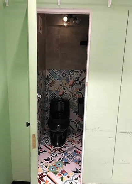 Ref#2992: A compact bathroom with light green walls, a black toilet, and patterned floral and geometric tiles on the floor and lower wall 6perfect for renting shop or office space.
