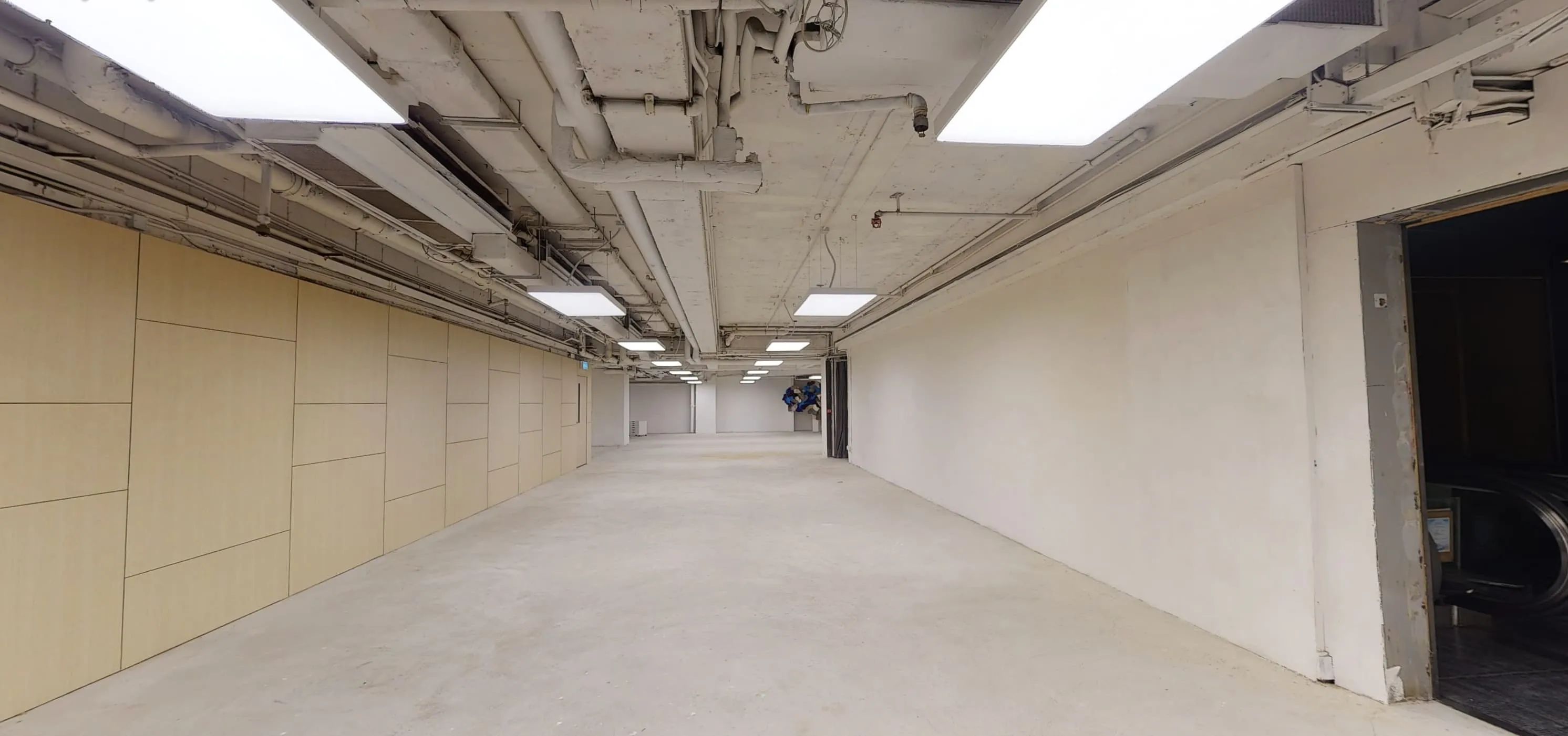 Wide empty hallway with white walls and beige panels in Central On Hing Terrace under fluorescent ceiling lights.