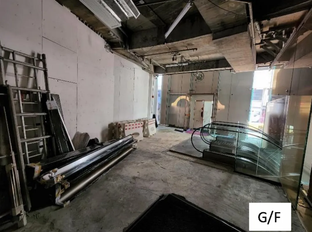 Ref#3011: Spacious, unfinished commercial unit ideal for shop or office rental, featuring exposed concrete, construction materials, ladders, and an escalator. Sunlit interior with glass door at the back. "G/F" labeled in bottom right corner.