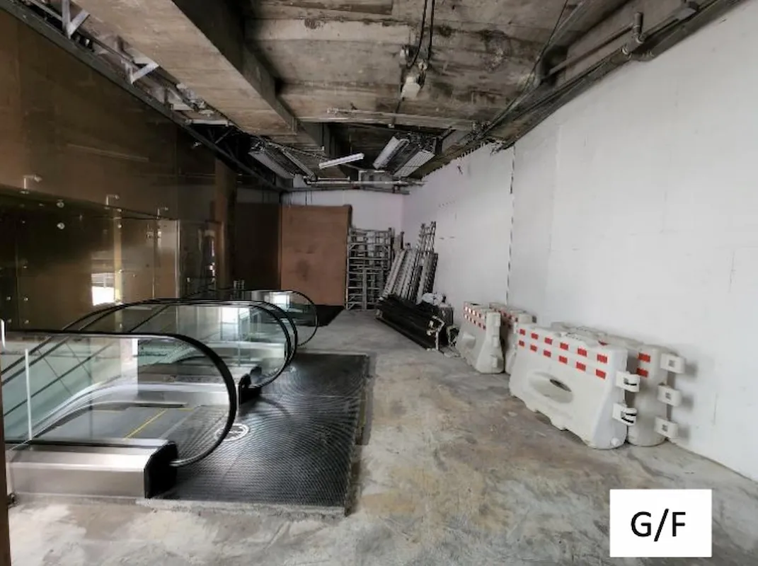 Ref#3011: An unfinished, industrial-style space ideal for shop or office rental, featuring exposed concrete ceiling, unused escalator, stacked materials, white safety barriers, and a G/F sign at the bottom right.