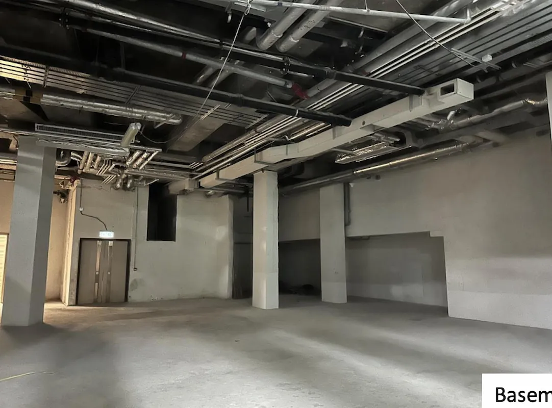 Ref#3011: An unfinished basement with concrete floors, exposed pipes and ducts, white walls, and a door with a windowdeal for those seeking office or shop space in an industrial-style setting.