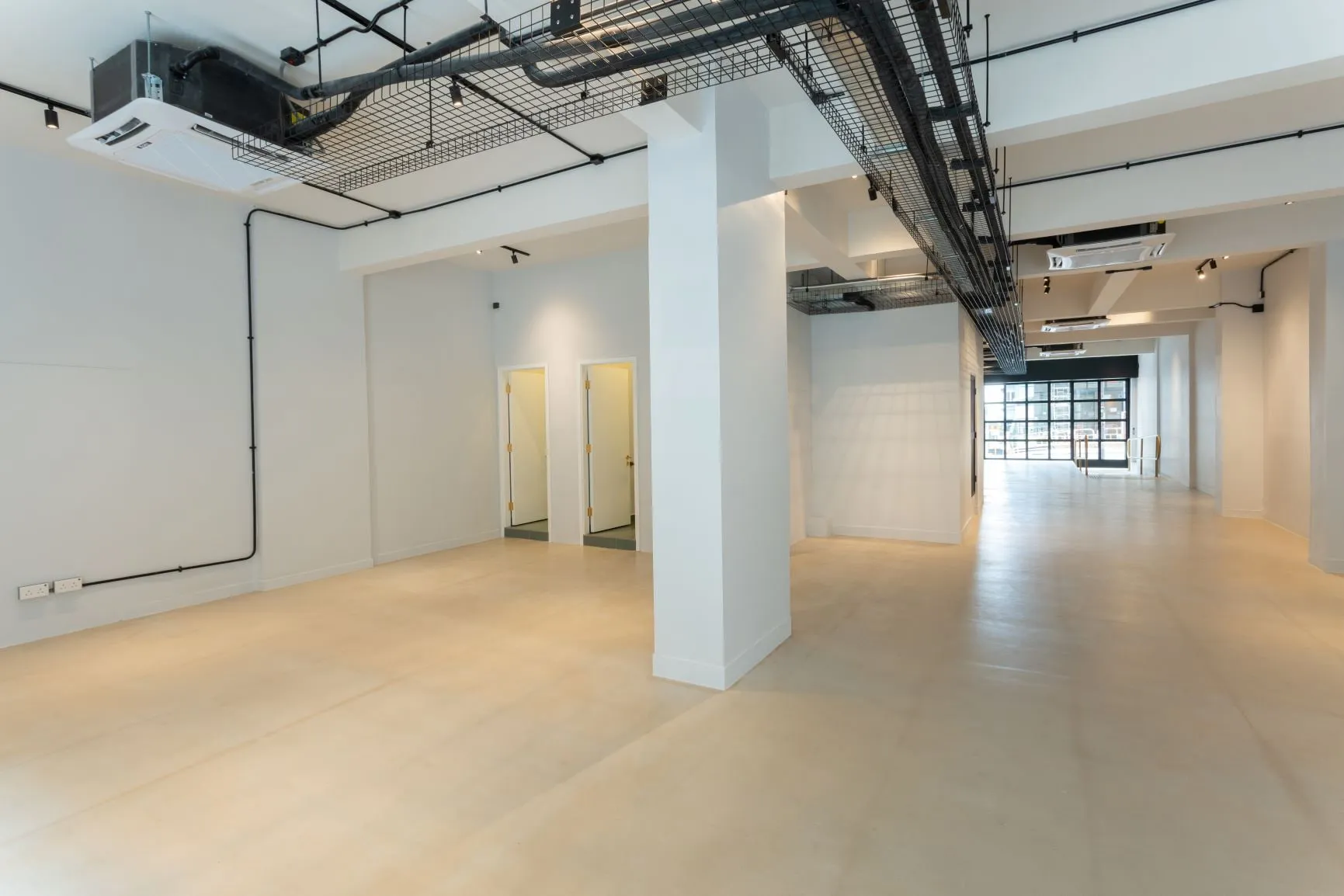 Empty room with white walls, exposed ceiling pipes, and doors in the background on Queen’s Road West.