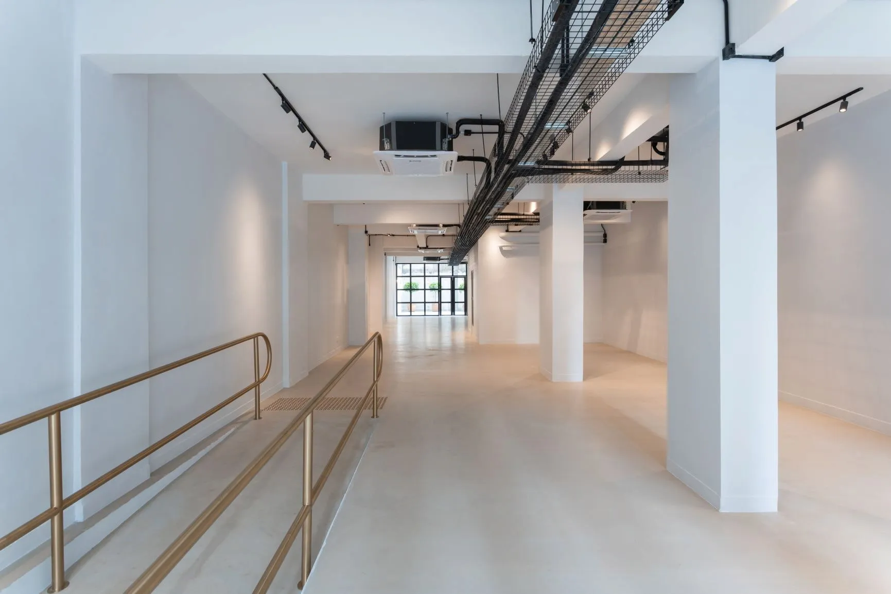 Empty white industrial space on Queen’s Road West with metal ramp, exposed pipes, pillars, and a large window.