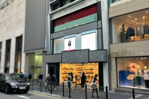 People stand outside a modern retail store on busy Queen’s Road Central with large display windows visible.