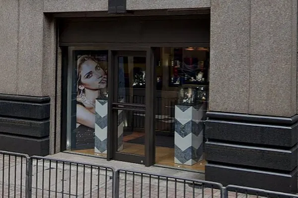 Ref#3526 features glass doors, a large jewelry poster on the left, and two decorative pillars at the entrance. Ideal for shop space rental. Metal barricades are positioned along the sidewalk outside the building.