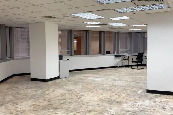 Ref#3224: A bright, modern office space with bare floors, white walls, and large windows. Desks and office chairs are set along one wall under overhead fluorescent lights ideal to rent for your workspace needs.