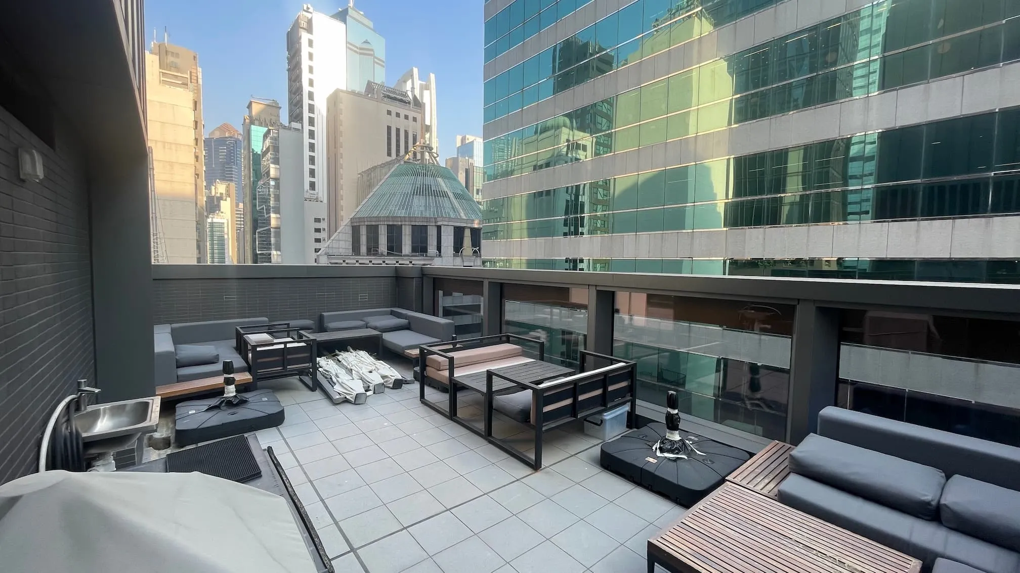 Rooftop patio on Central Wellington Street with black sofas, tables, chairs, and tall city buildings in the background.