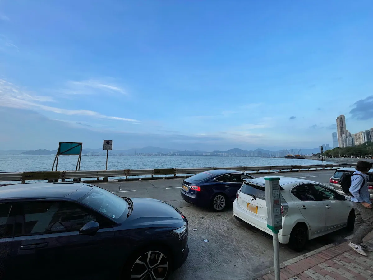 Ref#3608 offers a scenic coastal cityscape with parked cars on a waterfront road, clear blue sky, distant mountains, and skyline views	68ideal for office rental or enjoying local amenities. People gather near the sidewalk.