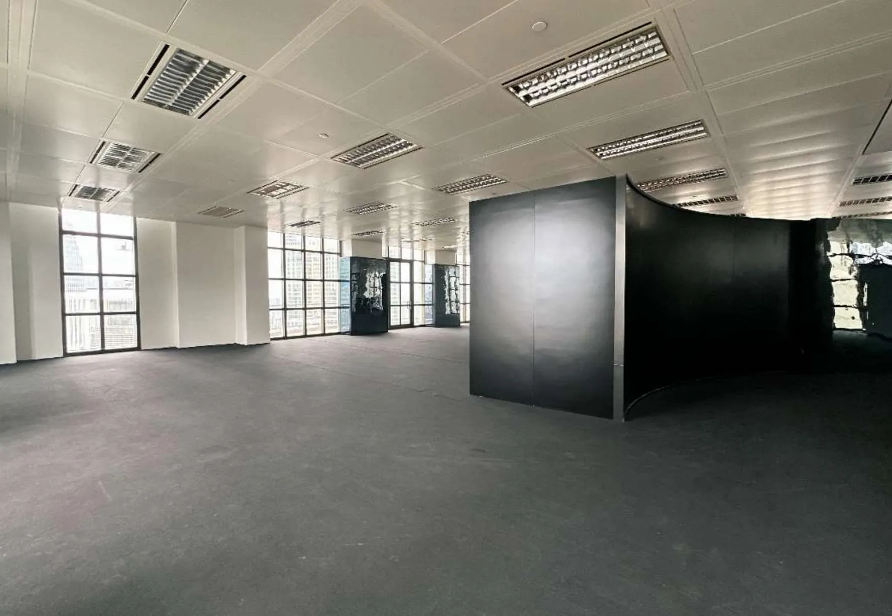 Ref#3609: A modern office space featuring large windows, white walls, dark flooring, a black curved partition wall, and ceiling lights—perfect for office rental.