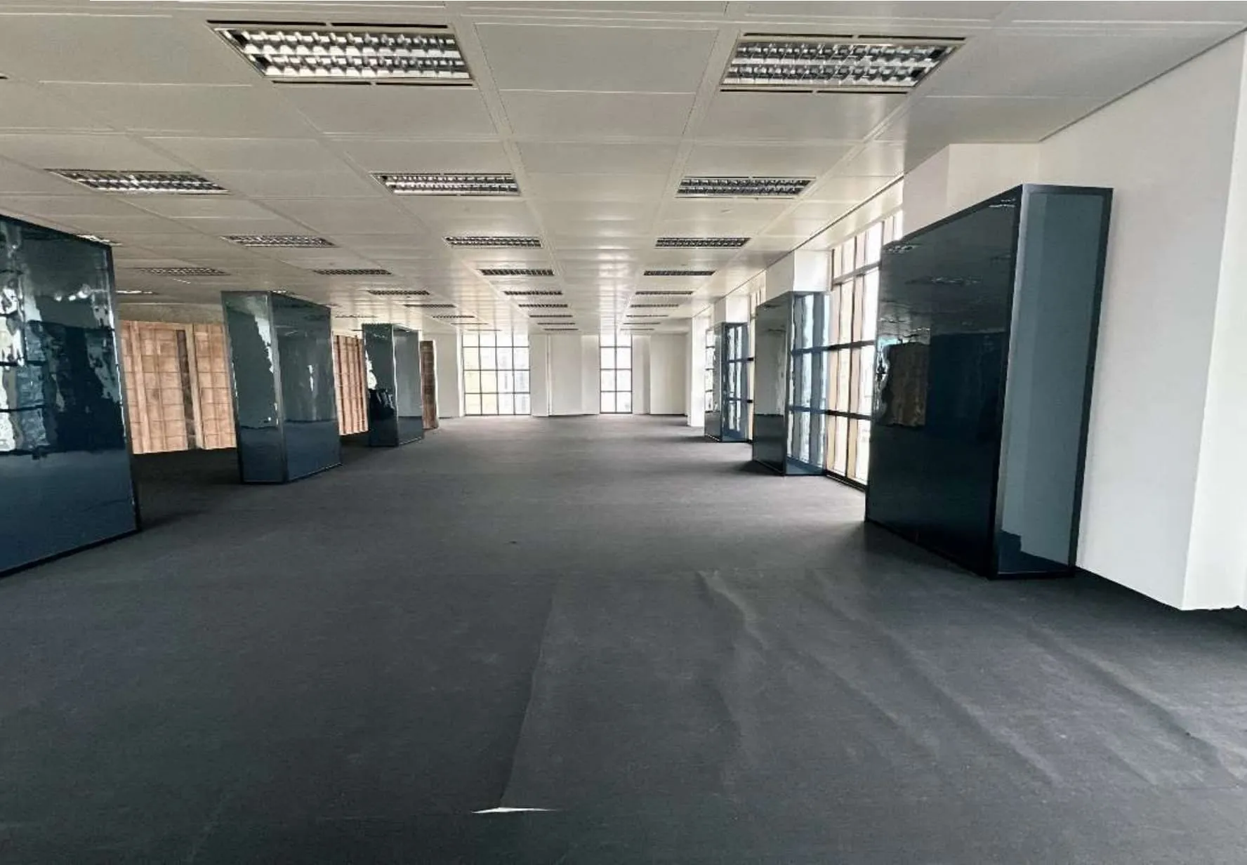 Office space Ref#3609 for rent with black carpet, tall dark blue partitions, floor-to-ceiling windows for natural light, and fluorescent ceiling lights—ideal office in a prime location.