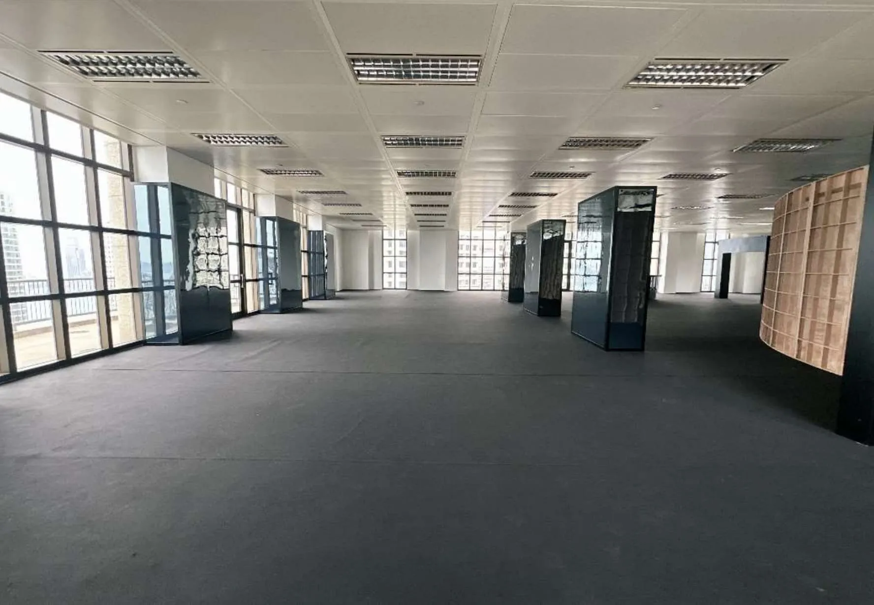 Ref#3609 is a spacious, empty office rental featuring large windows on the left for natural light, white ceiling tiles with fluorescent lights, and several glass partitions plus wooden panels along the right side.