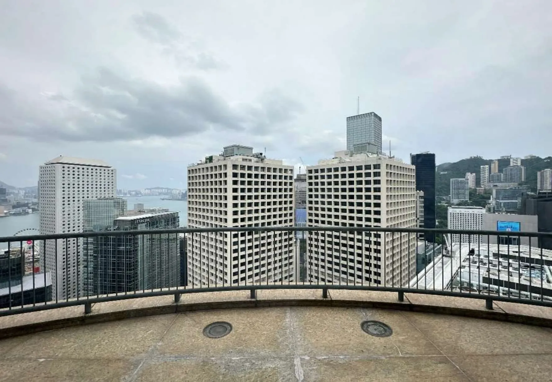 Enjoy a cityscape view from the balcony of Ref#3609, featuring tall, square-patterned buildings, water, and more—perfect for office or shop rental. Metal railing in foreground; cloudy sky above.