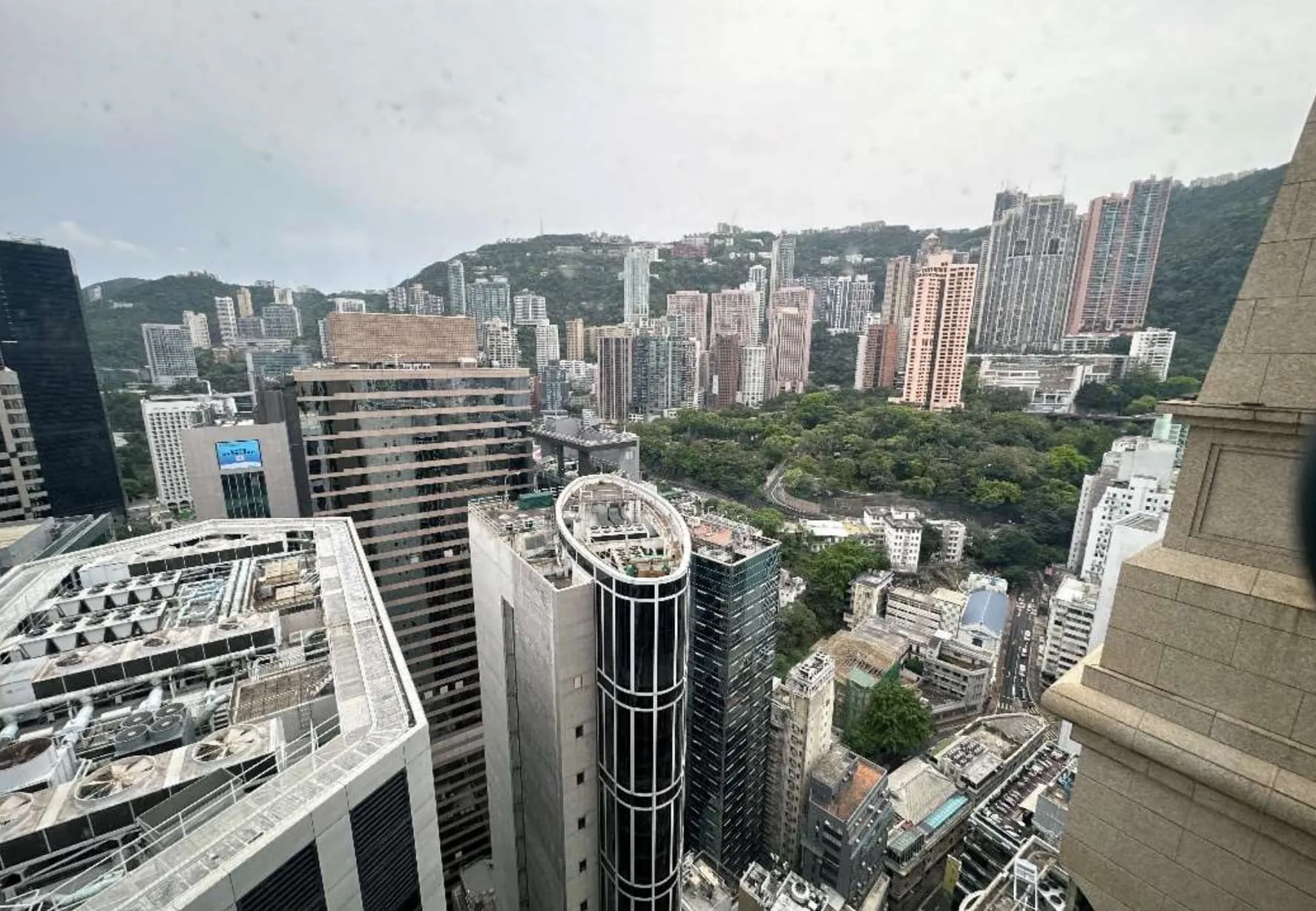 Aerial view of a cityscape with tall buildings, green trees, and hills under a cloudy sky—Ref#3609 offers an ideal location to rent office space or explore restaurant rental opportunities.