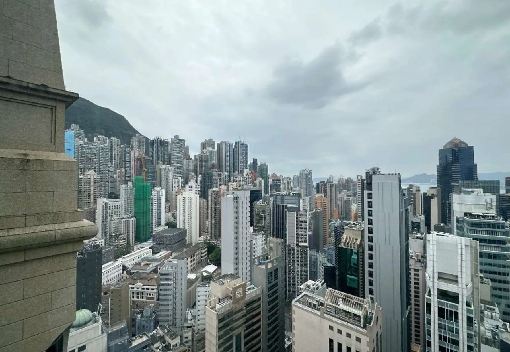 Ref#3609: Modern high-rise skyline under cloudy skies, with a mountain backdrop and partial stone building—perfect for renting office space that combines urban convenience with scenic views.