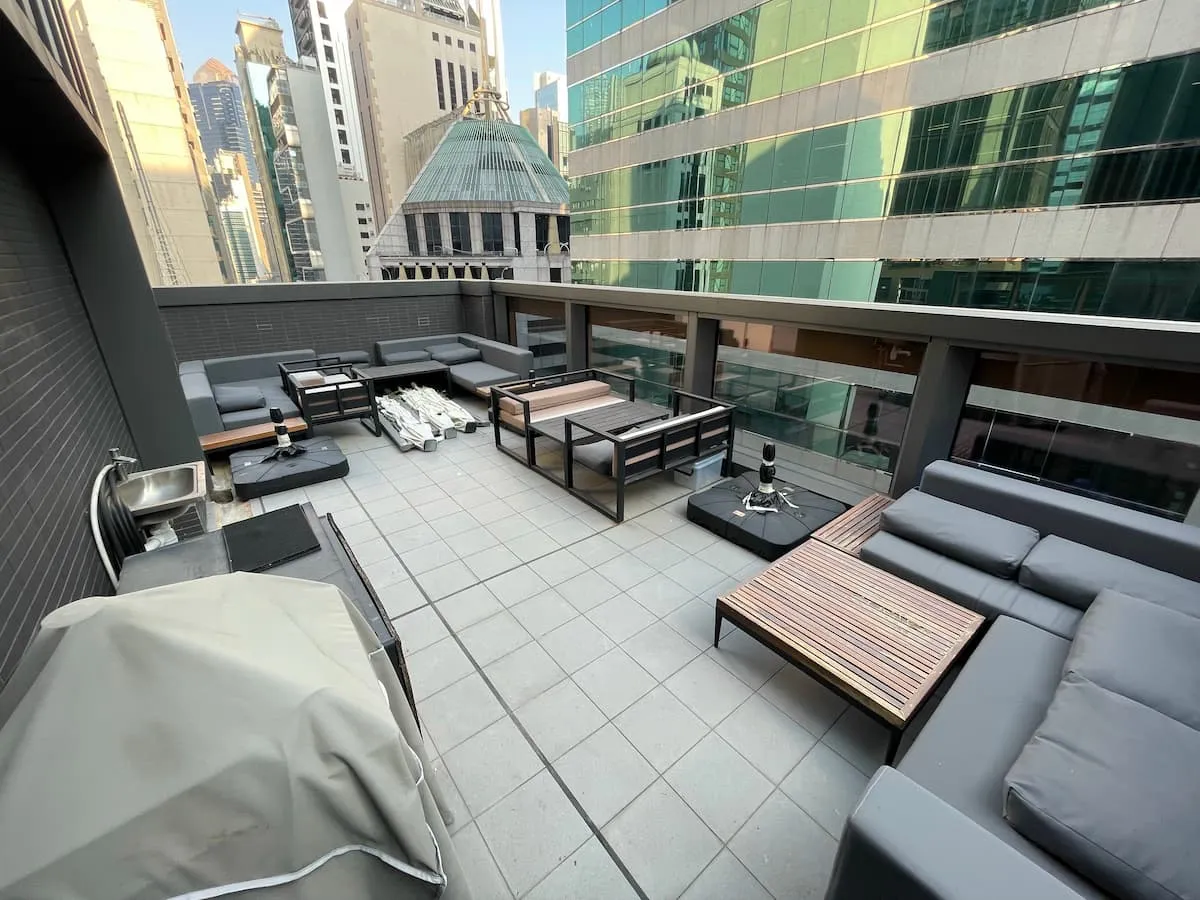 Rooftop patio on Wellington Street with gray sofas, wooden tables, covered grill, and city buildings in the background.