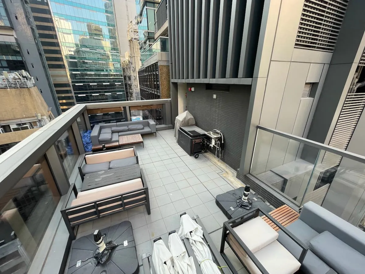 Rooftop patio on Wellington Street with gray sofas, tables, a grill, and city buildings in Central in the background.