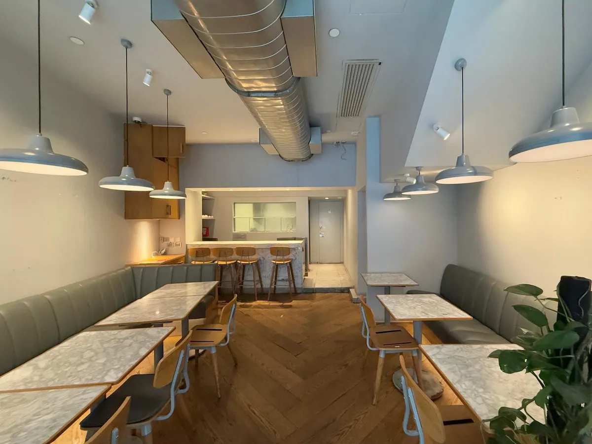 Ref#3636: Modern cafe interior for restaurant or shop rental—features marble tables, wooden chairs, gray bench seating, pendant lights, bar stool counter, herringbone wood flooring, and exposed air duct for a stylish finish.