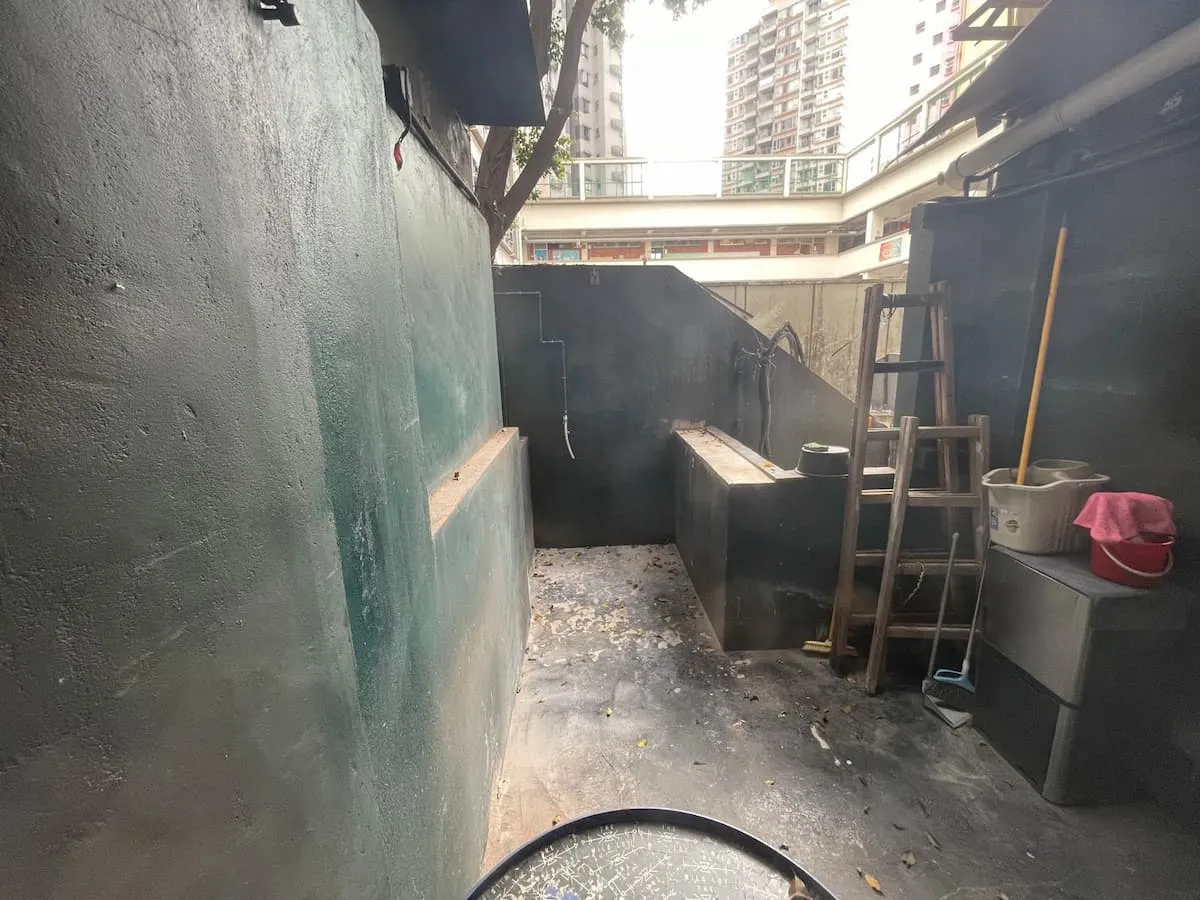 Ref#3622 features a compact outdoor concrete space with green walls, a raised sink, wooden ladder, and storage containersideal for renting as shop or office space. Tall residential buildings can be seen in the background.