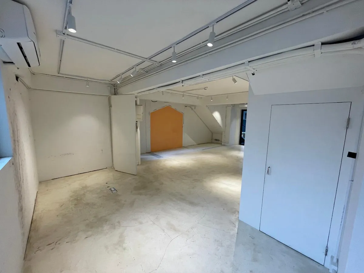 Ref#3622 features a spacious, empty room with white walls, a yellow accent wall, exposed ceiling pipes, track lighting, light-colored floors, natural light from the left window, and a white door on the rightideal for a shop or office.