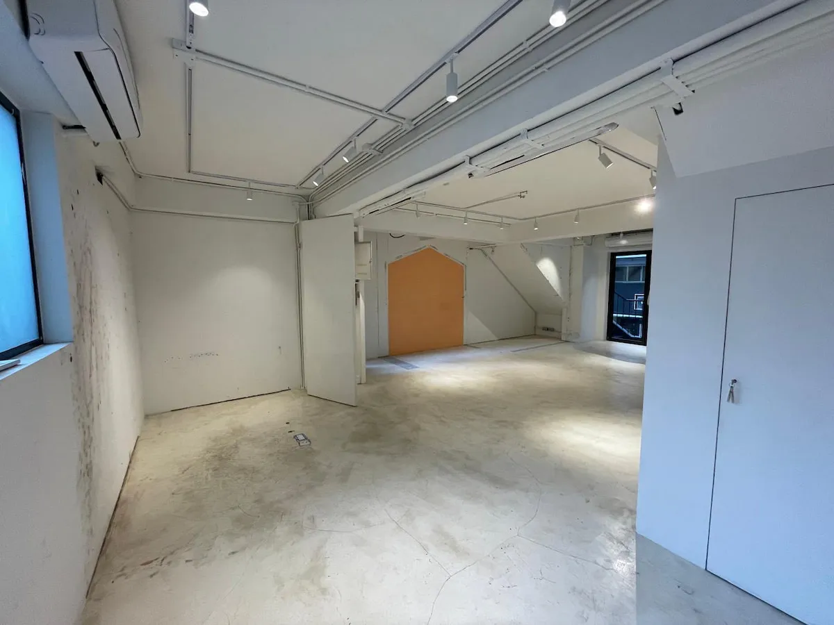 Ref#3622 offers a spacious, empty office rental with white walls, exposed pipes, track lighting, a large central pillar, a wooden accent wall, windows for natural light, and a polished concrete floor.