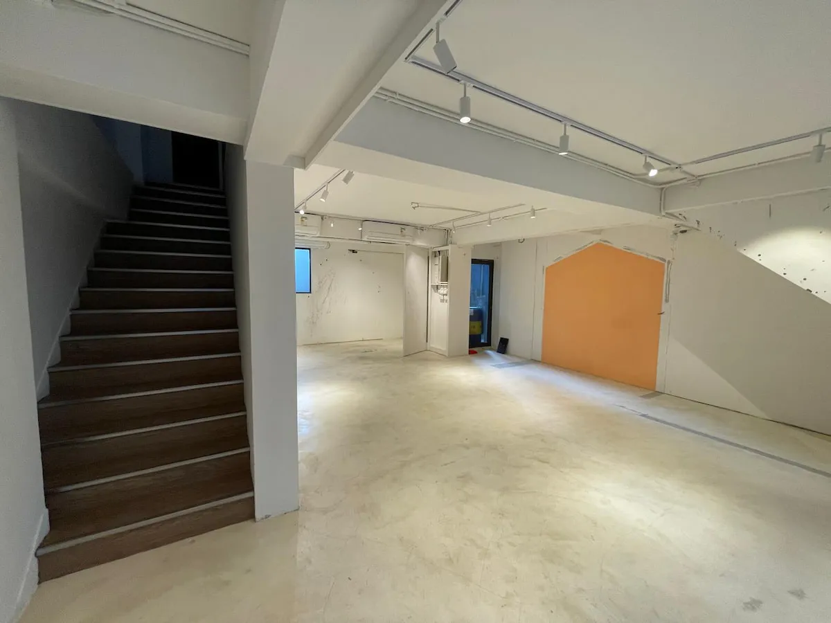 Ref#3622 features a spacious, empty room with white walls, polished light floors, a left-side staircase, an orange accent wall on the right, and ceiling track lightingperfect to rent as an office or shop.