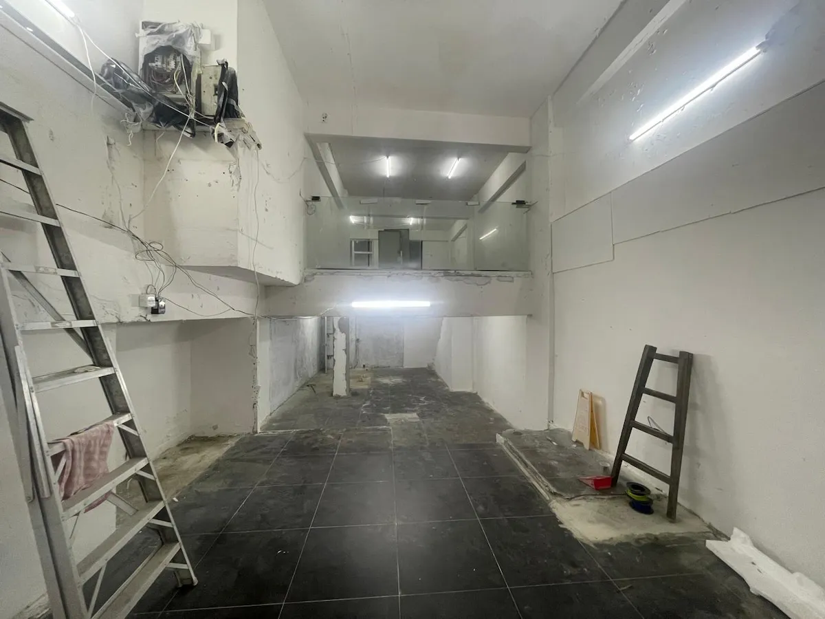 Ref#3623: A spacious, unfinished room with white walls, exposed wiring, two ladders, tiled floors, a split-level area, and fluorescent lightsperfect for renting as an industrial-style shop or office under renovation.