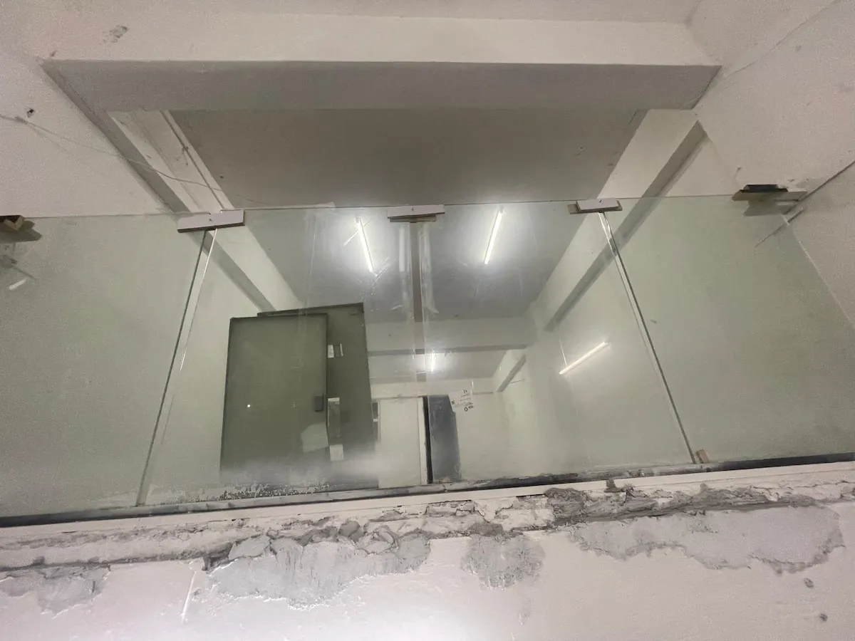 Ref#3623: Glass railing with metal brackets, perfect for balconies or mezzanines in unfinished interiorsideal for office or retail rental spaces featuring exposed concrete and fluorescent lights.
