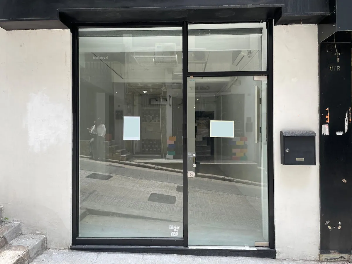 Ref#3624 features a glass storefront with two frosted square stickers on the door and a black mailbox to the right, available to rent for office, shop, or restaurant use. The spacious interior reflects the street and nearby building in the glass.