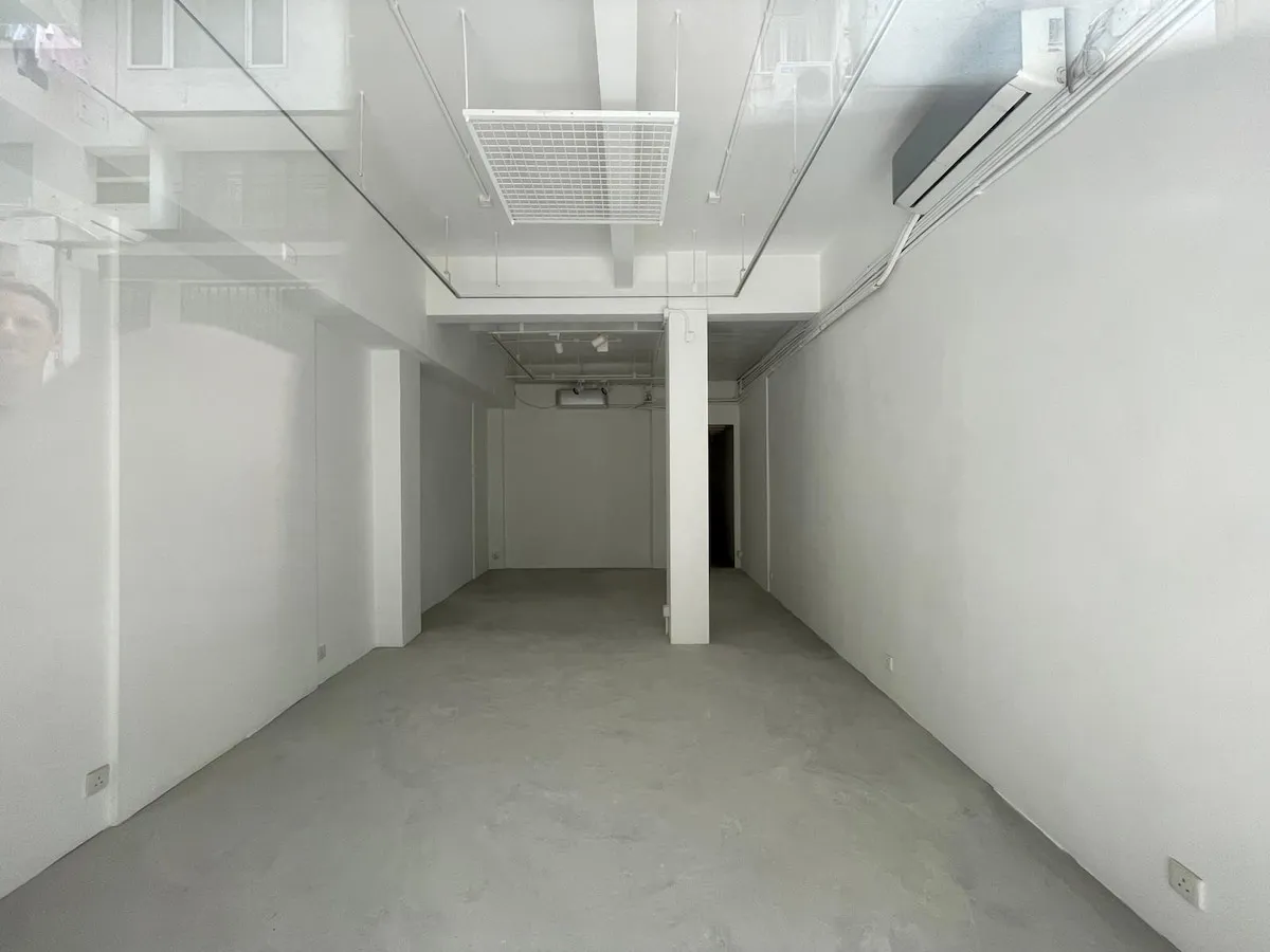 Ref#3624: An empty, narrow room with white walls, concrete floor, high ceiling, overhead lights, air conditioning unit, and glass panels near the ceilingideal to rent as an office or shop.