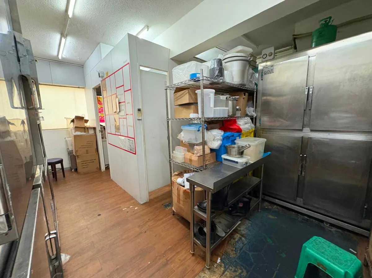 Ref#3625 features a commercial kitchen storage area with metal shelving, containers, boxes, and supplies near large stainless steel refrigerators. Wooden floors and open doorways create an ideal space to rent for a shop or restaurant.