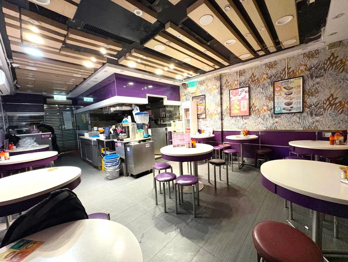 Ref#3625: A modern, brightly lit restaurant featuring purple and white decor, round tables, stools, an open kitchen, menus and condiments on display. The spacious venue is ideal for those seeking to rent restaurant space.
